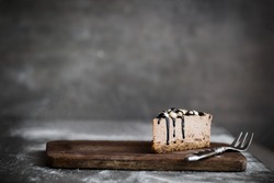 Cut of raw chocolate mousse cake with cashew, hazelnuts and dark chocolate glaze topping on a wooden and grey background. Vegan sugar gluten free dessert. Dark food photography. Copy space, horizontal