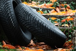Pair of brand new all weather tires lying on wet asphalt covered in fallen golden leaves in rainy autumn season. 