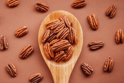 Pecan nuts close-up in a wooden spoon on a brown background.shelled pecans. Healthy fats. Keto diet ingredient. Nuts and seeds. Useful healthy snack.