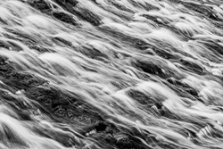 Long exposure of water flowing over algae covered rocks at Lopwell Weir, Plymouth, Devon