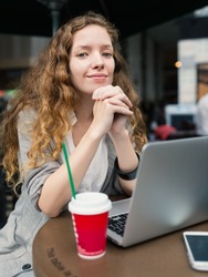 Young business woman with hot beverage and laptop inside coffee store. 