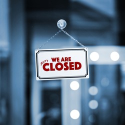 WE ARE CLOSED sign board through the glass of store window. Filtered image.