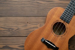 Top view at hawaiian brown guitar ukulele on dark wooden background. Country lifestyle. Ukulele body, soundhole, and fret. Copy space. Folk music instruments.