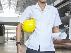 The man holding a yellow safety hat holding a paper with the plan for the building.
