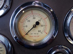 a round metal pressure gauge with a shiny chrome surround on a control panel with other meters