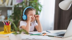 sad little girl, schoolgirl wearing headphones, uses laptop to study at home. child is bored to learn and gain knowledge remotely. student wants to go to school. digital concept e-learning.