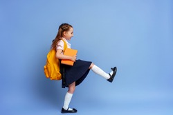 Cute happy kid in uniform. raises his leg high and runs on purple background. child with backpack. little girl is ready for school. Dynamic images that go back to conceptual school. holidays begin.