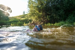 Happy boy in swimming glasses swims in the river in the summer at sunset. A child enjoys a summer children's holiday on the shore of the lake. Active holidays. Dynamic Image