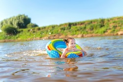 Happy girl swims on an inflatable circle in the river in summer at sunset. A child enjoys a summer children's holiday on the shore of the lake. Active holidays. Dynamic image
