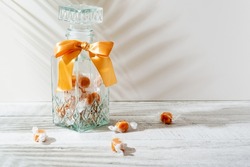 Beautiful transparent glass mason jar with orange bow and a few caramel candies on light background. 