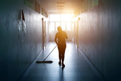 Janitor woman mopping floor in hallway office building or walkway after school and classroom silhouette work job with sun light background. Poor people working job.