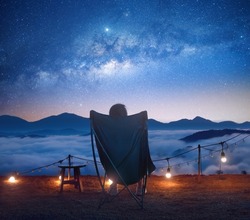 woman in a camping chair looks at the starry sky and the sunrise in the mountains. Dalat, Vietnam. Focus only in the center