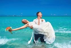 Groom holding bride in his arms by the sea