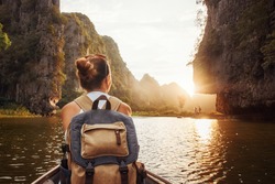 Woman with backpack swims on boat among karst mountains to meet her friends. Tam Coc,  North of Vietnam.Travel and active lifestyle, summer holiday concept.