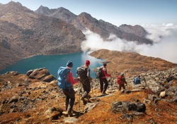 Group of tourists with backpacks descends down mountain trail to lake during a hike in the national park Lantang, Nepal.Beautiful inspirational landscape, trekking and activity.