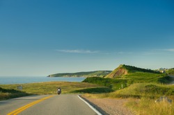 Cabot trail coastline in Cape Breton Island, Nova Scotia during the summer season. A motorcycle is visible along the road.