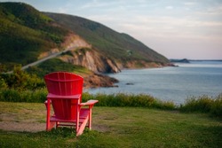 A red Adirondack chair facing the Cabot Trail in Cape Breton Highlands National Park, Nova Scotia, Canada on a beautiful summer day