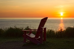 Sunset view from the Cabot Trail in Cape Breton Highlands National Park, Nova Scotia, Canada. A single red Adirondack chair is visible