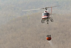 Fire Fighting and Rescue Helicopter with Bambi Bucket Carrying Water to put out a Forest Fire with Mountain Background, Copy Space