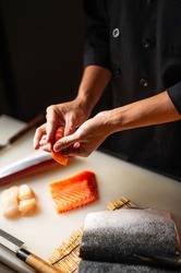 Closeup of chef hands preparing japanese food. Japanese chef making sushi at restaurant. Young chef serving traditional japanese sushi served on a cuting board in lighting studio . 