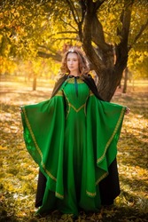 A beautiful girl in a medieval green dress with golden braid. Queen in a cloak and a blio dress in the autumn forest. historical image