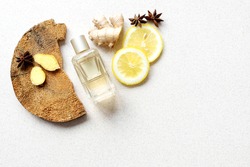 glass perfume bottle with lemon wedges, anise stars, wood bark and ginger fragments on beige background. fresh, woody, spicy unisex scent concept. Copy space