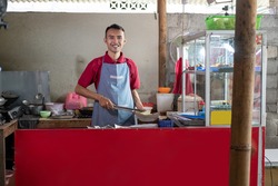 The stall waiter stands holding tongs while preparing the side dishes ordered by the customer at the shop