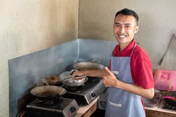 the male waiter smiles with a thumbs up while frying side dishes for customers at the stall