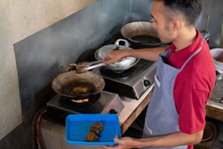 the cook lights the stove to fry the side dishes for the customers at the food stall