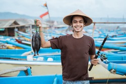 Happy young fisherman on the beach holding his catch fish and shows in front of his boat