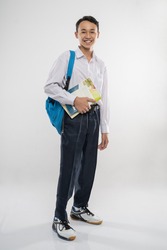 a boy standing in junior high school uniform smiling holding a book and school bag on an isolated background