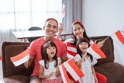 portrait of happy asian family celebrating indonesian independence day at home wearing red and white with indonesia flag