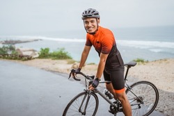 male asian cyclist with red and black jersey standing on his bike