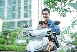 Smiling asian man using a cellphone while riding a motorcycle