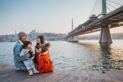 happy asian family sitting on the side of bosphorus looking at beautiful sunset in istanbul turkey