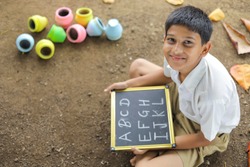 Indian child writing A B C D alphabet on Chalkboard
