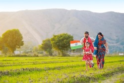 Indian little girl running and waving national flag with father and mother at agriculture field