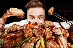 Crazy hungry man eating mix grill meat. Emotional content for restaurant promo. Cheat day. Meat lover. Lamb chops, chicken tikka, kebab, lamb, beef steak. 