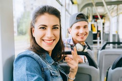 Young smiling multicultural couple, handsome guy and young woman talking while sitting in the city tram. Youth millennial teenager people taking selfie in public transport. Acquaintance concept.