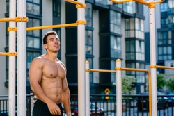 Positive topless muscular athlete under sports bar after pulling up on sportsground during workout.Naked torso man looking away, relaxing after exercises. Sport, lifestyle and people concept.