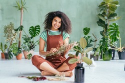 Young woman cultivating home plants.Small business.Sensual mixed race female florist with flowers in hands against background of indoor plants. Life lover, zero waste, inspiration, summer mood concept