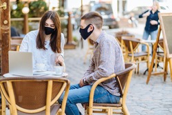 Student youth hipster man and young woman in facial masks drinking coffee at an outdoor bar cafe or restaurant. New normal concept reopening after quarantine concept.