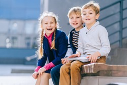 Portrait of happy blond little boy with other kids on blurred background.Three different age children with book sitting on the bench in the schoolyard at the day time.