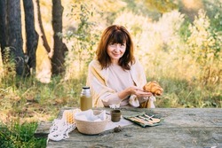 Sustainable, ethical, plastic free, cozy slow lifestyle. Plastic free concept. Mature woman in knitted sweater having picnic outdoor with tea in thermos and fresh croissant, net eco bag at autumn.