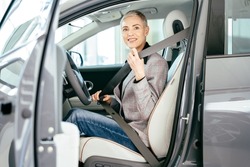 Eco car sale, portrait of smiling young caucasian woman sitting alone on driver seat of electric car with fasten belt while driving modern car. Lifestyle and success concept.
