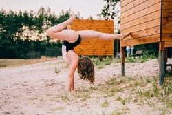 Young teen girl in swimsuits doing a handstand gymnastic workout on the beach. Upside down handstand happy smile sport young woman outdoor, full lenght.