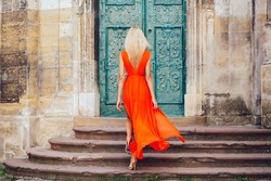 Woman in orange dress climbing stairs outdoors in old city. Back view.