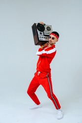 cheerful fashionable man wearing a red sports suit dancing jumps with a retro tape recorder. interesting and fervent style of the 90s.