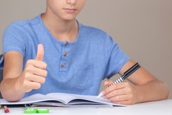 Boy hand holding pen in left hand and writing in a notebook, doing homework. Thumb up hand gesture. Left Handers Day