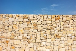 Old brown masonry wall of stones and blue sky background. Low angle view